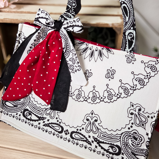 White tote bag with black paisley pattern and red polka dot ribbon on a wooden surface
