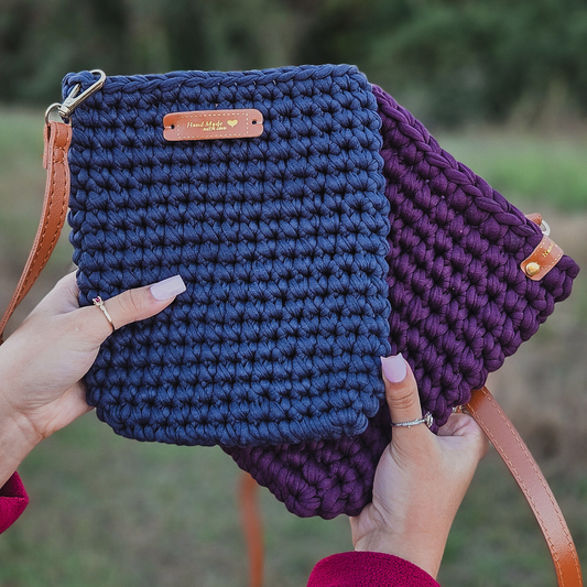 Two hands holding a blue and purple crocheted bag with a visible brand label.